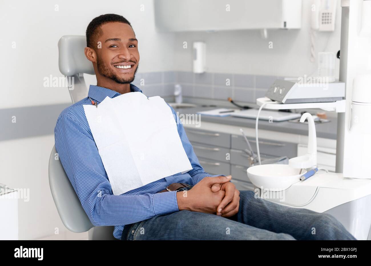 Happy black guy sitting on dentist chair, attending dental clinic Stock