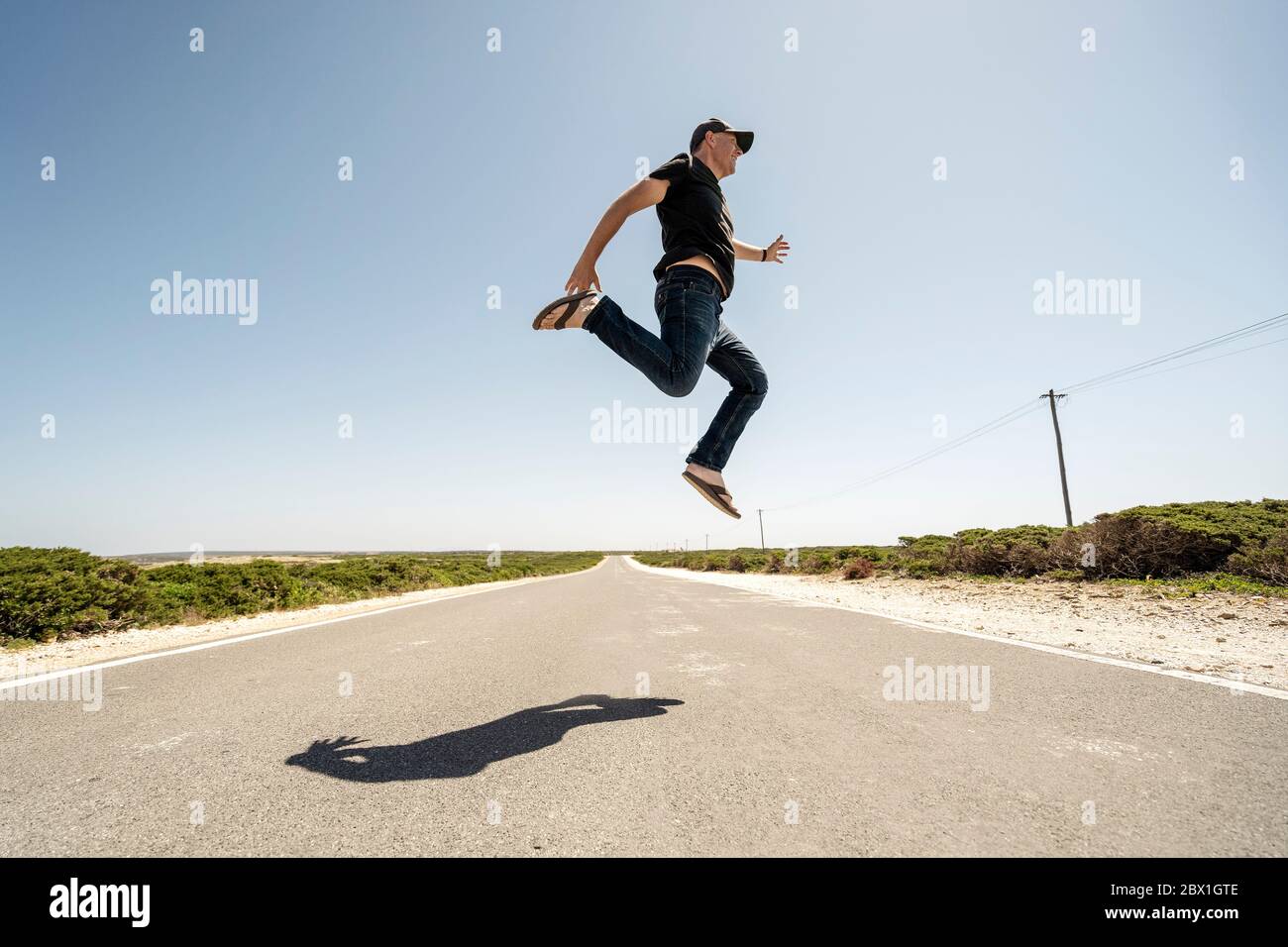 Man happily jumping high above the road in the wilderness Stock Photo