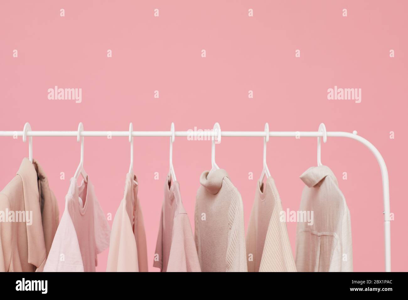 Close-up of dresses and shirts hanging on the rack isolated on pink background Stock Photo