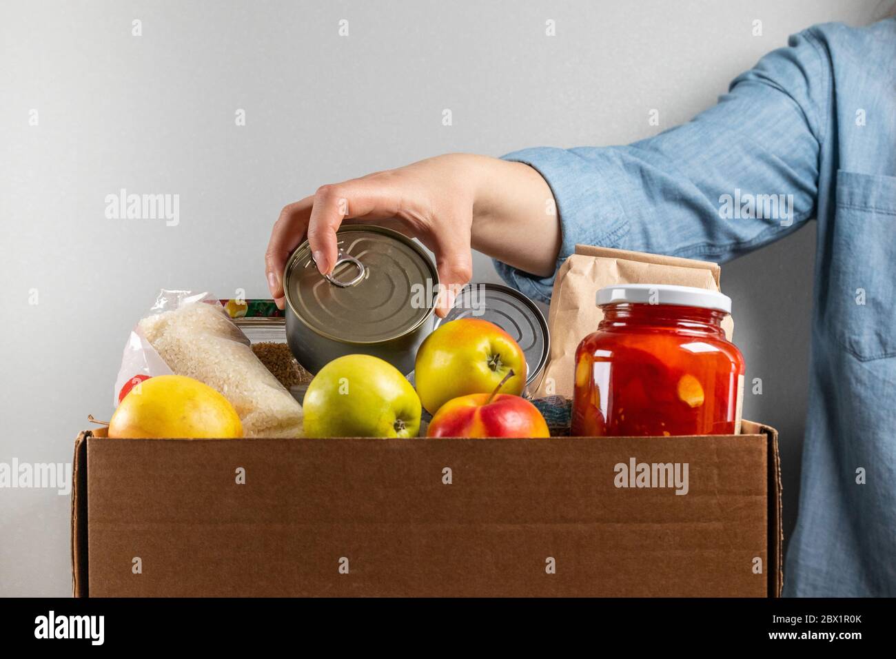 Female hand puts tin can in food donation box Stock Photo Alamy