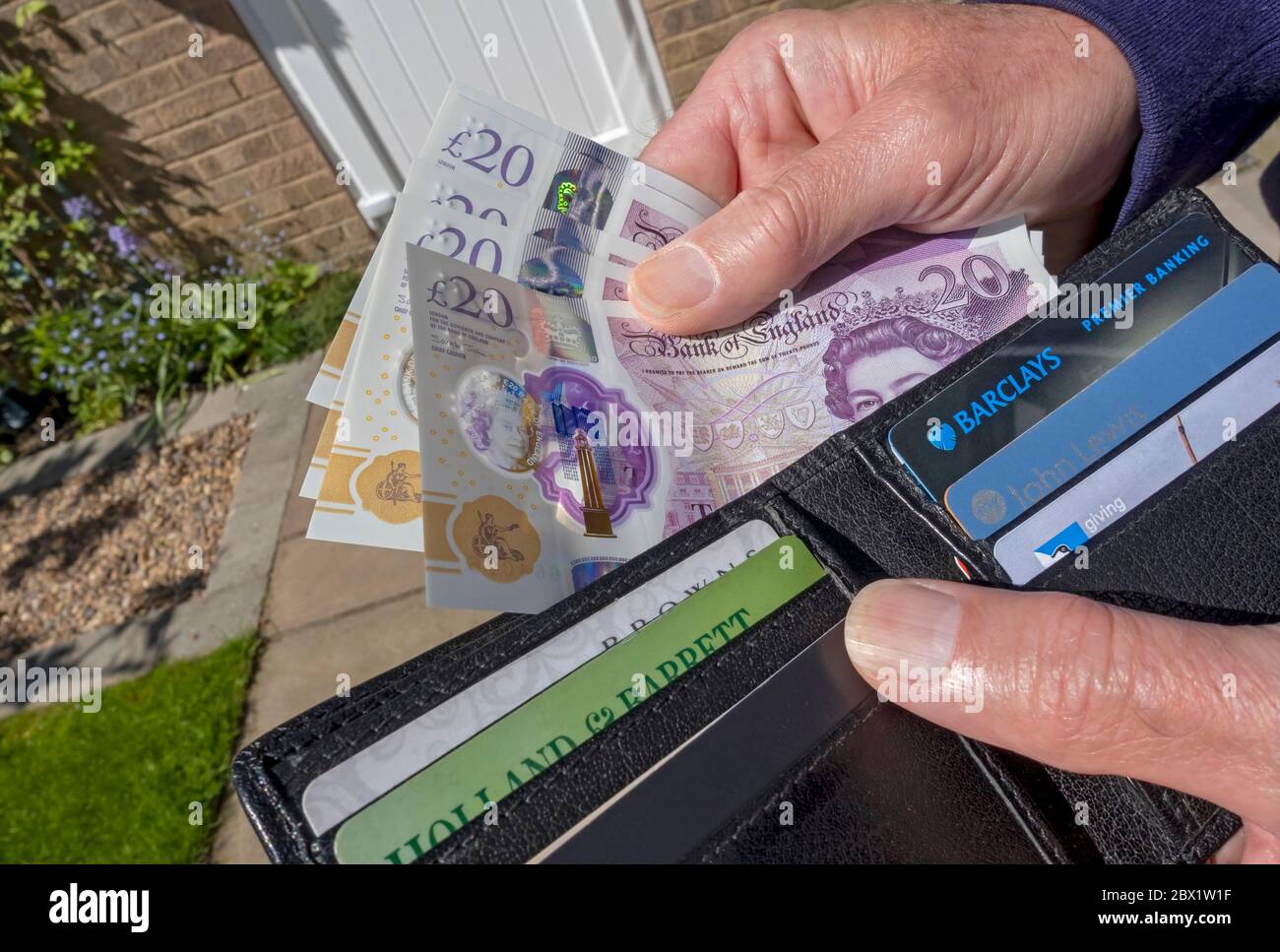 Close up of man person taking paying English £20 twenty pound notes cash money from out of wallet England UK United Kingdom GB Great Britain Stock Photo