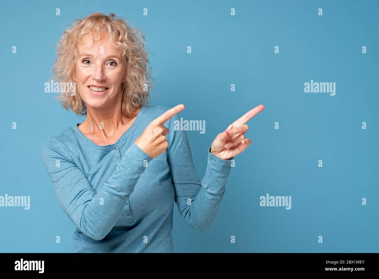 mature woman with dyed blonde hair smiling cheerfully and pointing on copyspace. Stock Photo