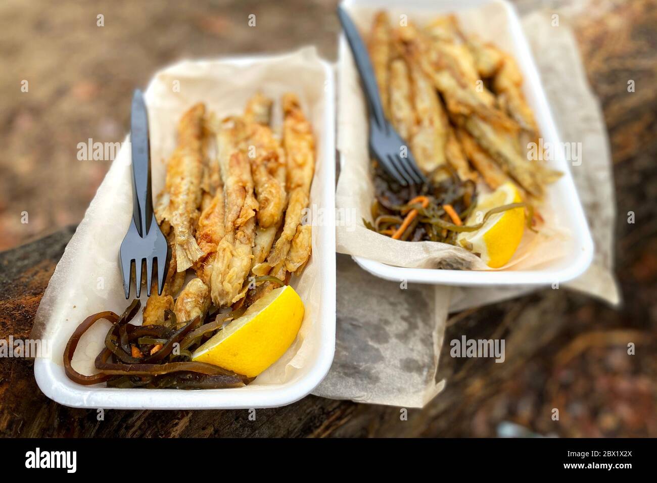 Fried smelt on piece of baking paper on brown wood in on a picnic in the forest , closeup. Small fish next to a lemon and sea kale. View from above. Stock Photo