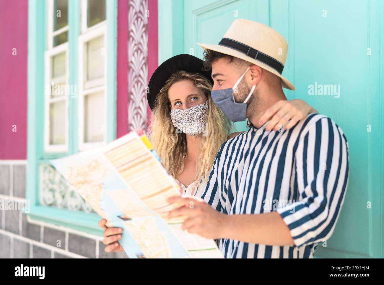 Young couple wearing face mask and holding travel map - Travelers people enjoying first trip after corona virus outbreak Stock Photo