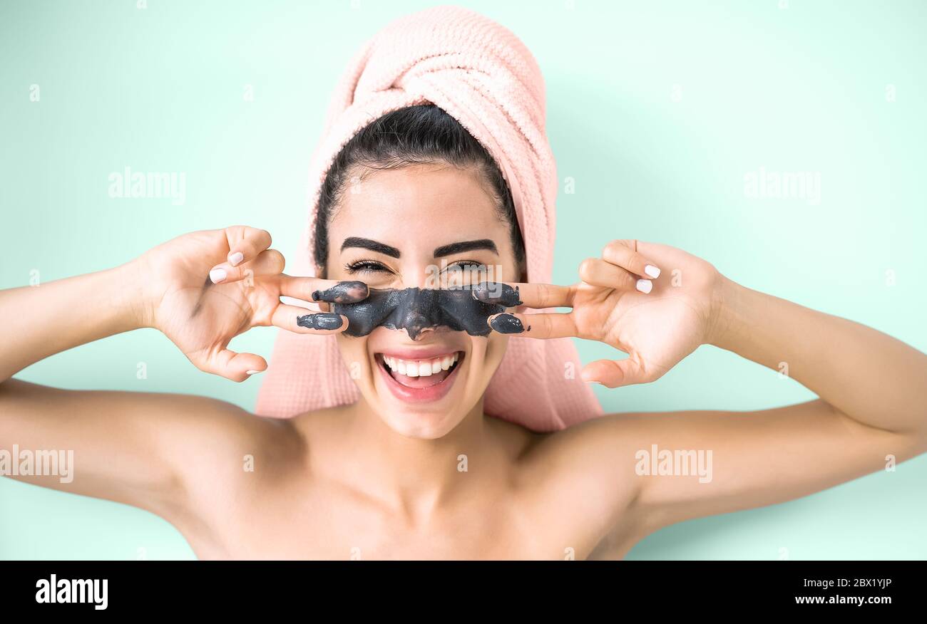 Happy smiling girl applying facial charcoal mask portrait - Young woman having skin care cleanser spa day Stock Photo