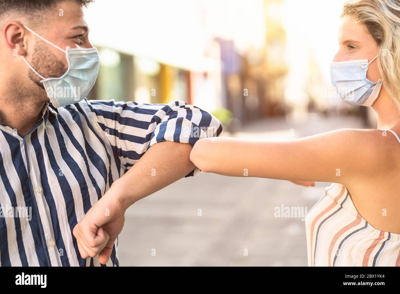 Young friends wearing face surgical mask doing new social distancing greet with elbow for preventing corona virus outbreak Stock Photo