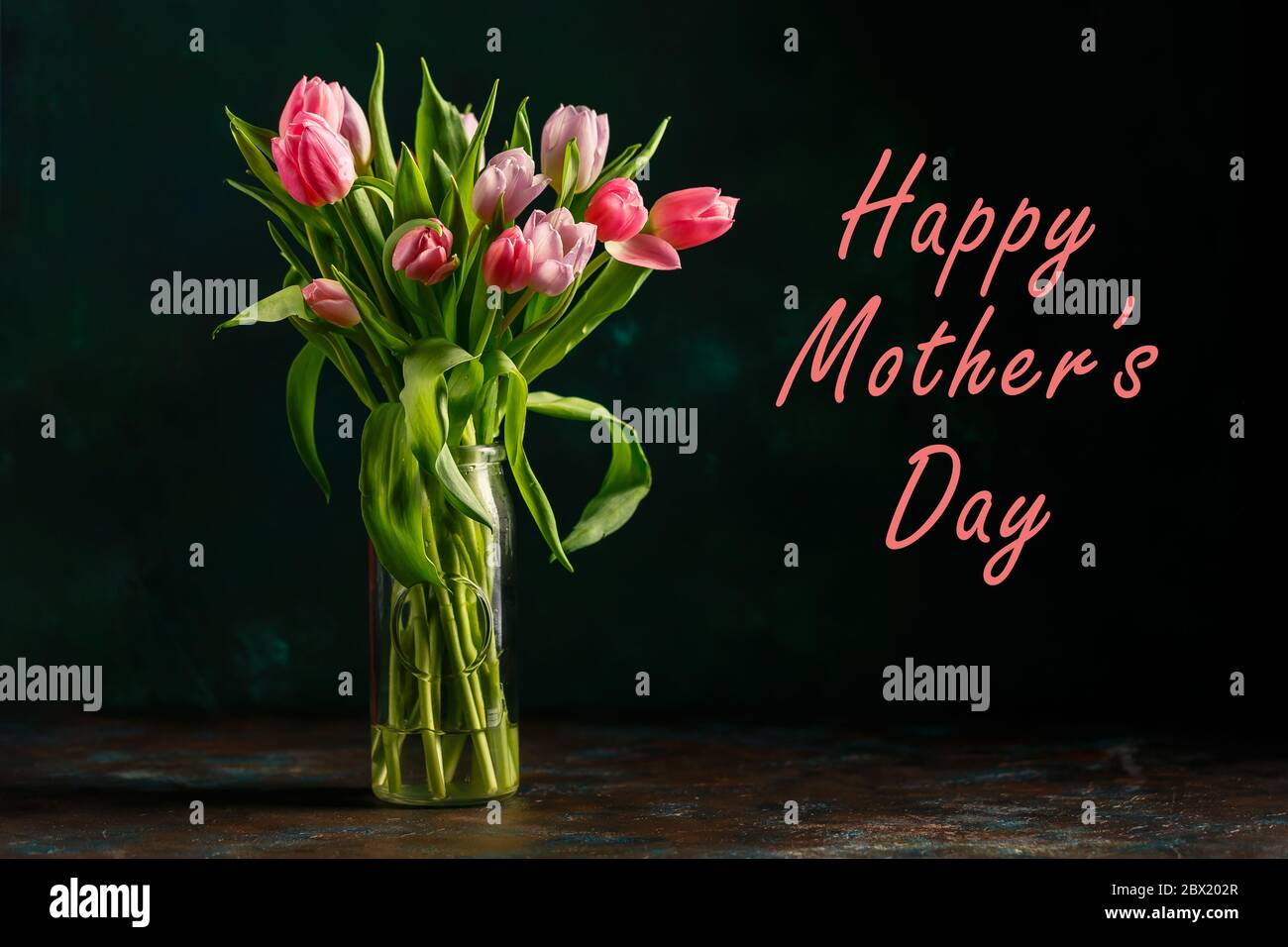 Bouquet of pink and lilac tulips in a glass vase on dark green ...