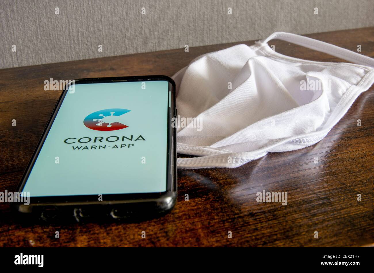 Zittau, Saxony / Germany - June 4th 2020: German Corona Virus Warn App for COVID-19 tracing with white face mask on wooden surface. The new normal, it Stock Photo