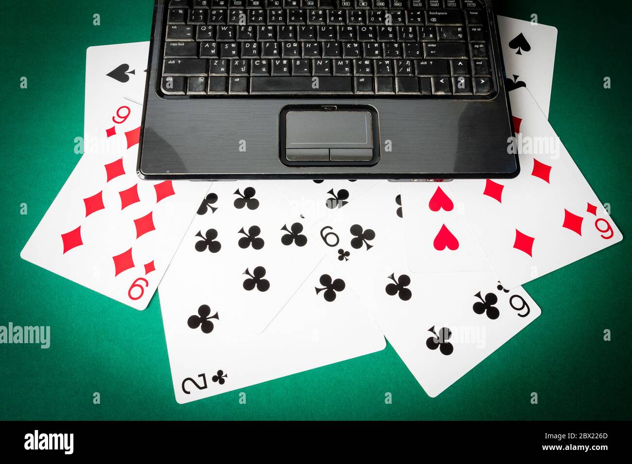 Laptop with playing cards on green background. Stock Photo
