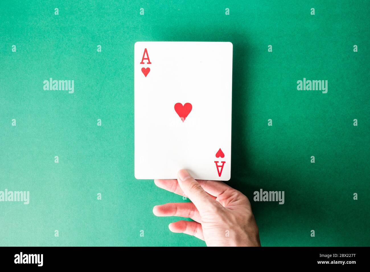 Hand holding a playing card on green background Stock Photo - Alamy