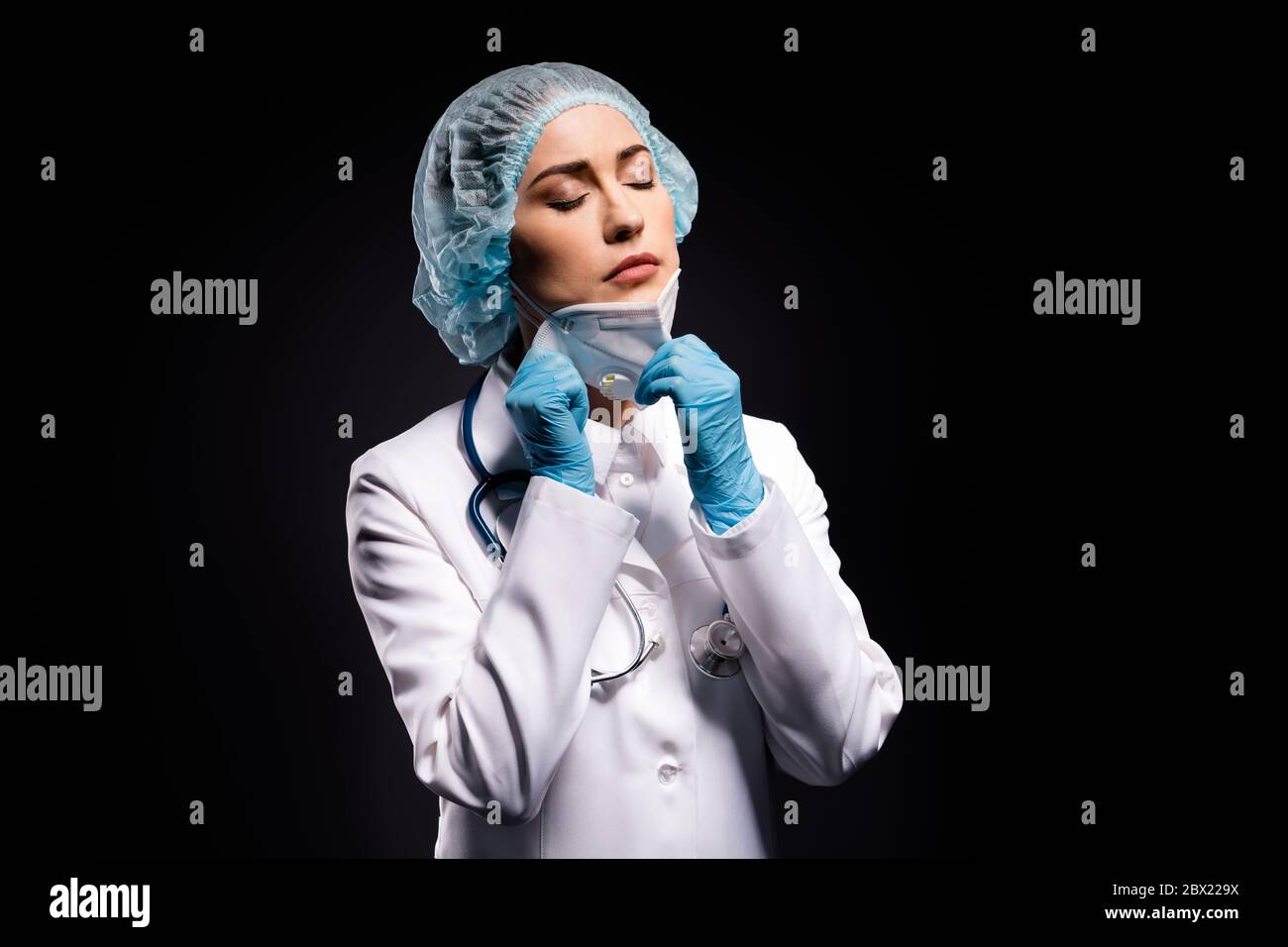 Photo of tired lady doc taking off protective mask after late operation breathing fresh air eyes closed wear gloves lab white coat surgical cap Stock Photo