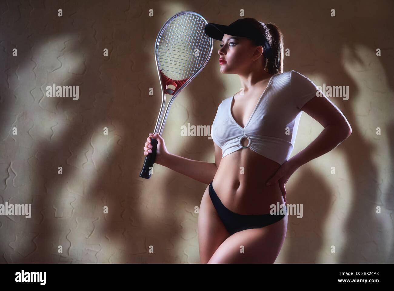 Young beautiful woman with tennis racquet in profile against a grunge wall with a striped shadow Stock Photo