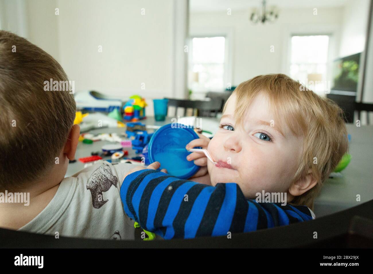 Blue-eyed toddler boy at kitchen table looks over shoulder with milk Stock Photo