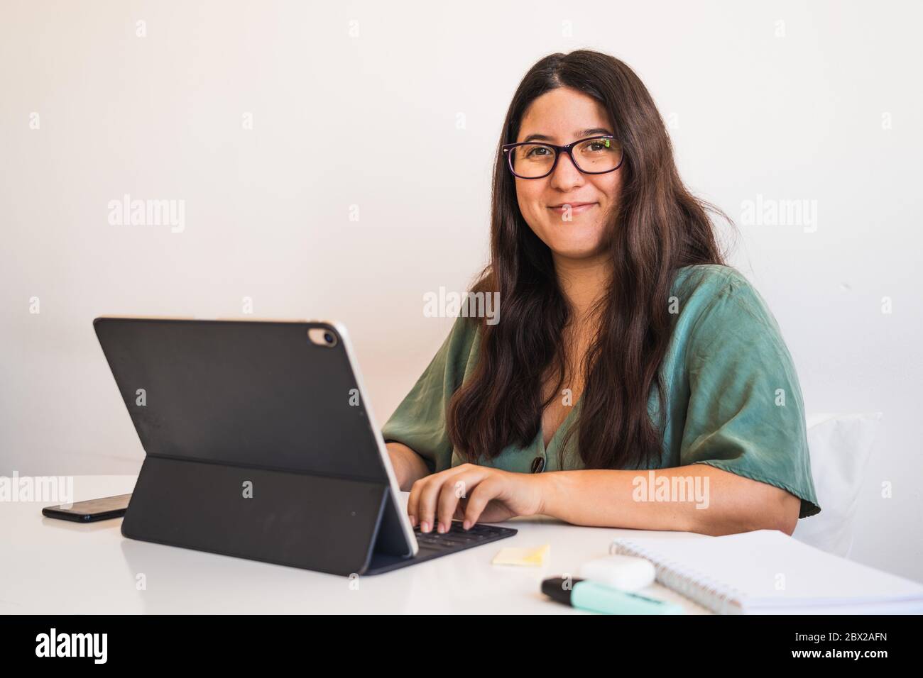 Young spanish brunette wearing glasses teleworking with her hybrid tablet laptop adapting her business to the new normal after the covid 19 global pan Stock Photo