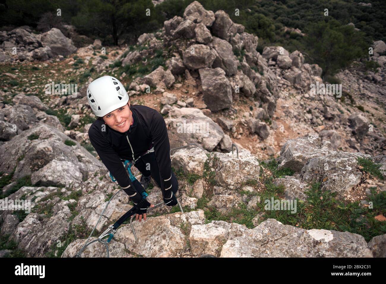 Concept: adventure. Climber woman with helmet and harness. Looking at camera happy. Anchored to the high natural wall. Smiling. Doing via ferrata in t Stock Photo