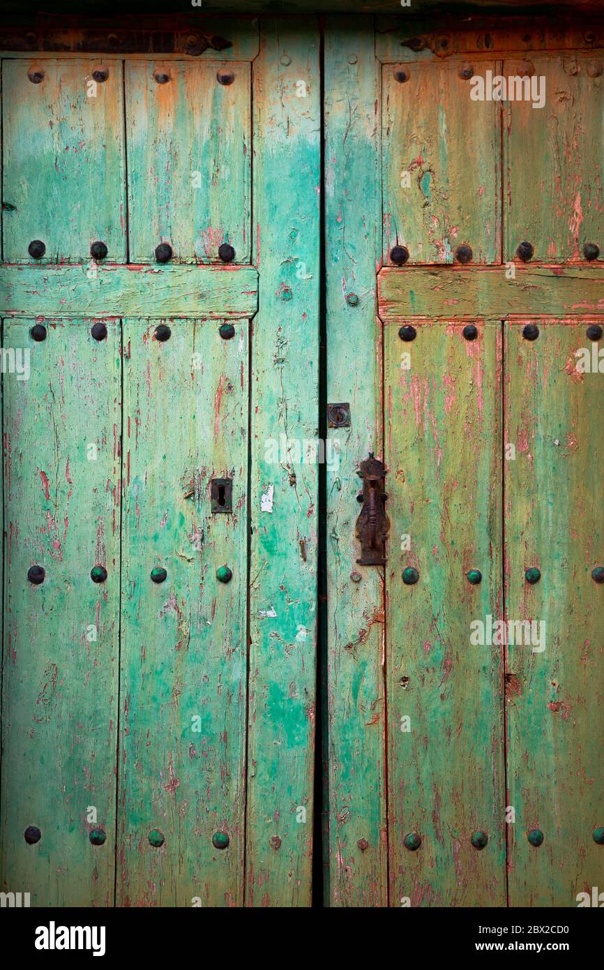 Old rustic wooden door with different layers of cracked paint in green and orange colors Stock Photo