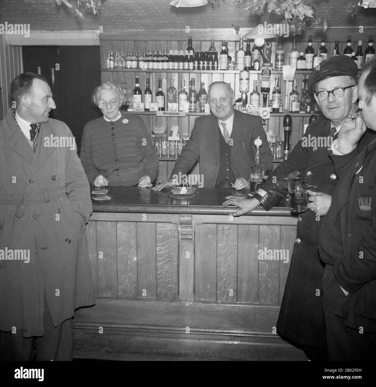 1960, in this historical picture, local men are enjoying a pint at the bar a pub with the landlord and his wife standing behind the counter, England, UK. Stock Photo