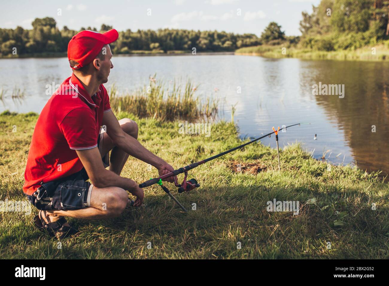 A man fisherman on the river bank catches a fish - pulls the line on the  reel Stock Photo - Alamy