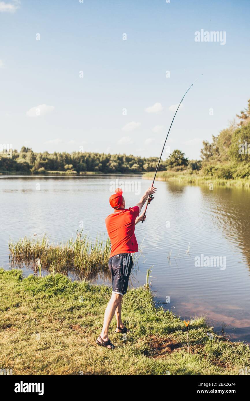 A man fisherman on the river bank throws a fishing pole Stock