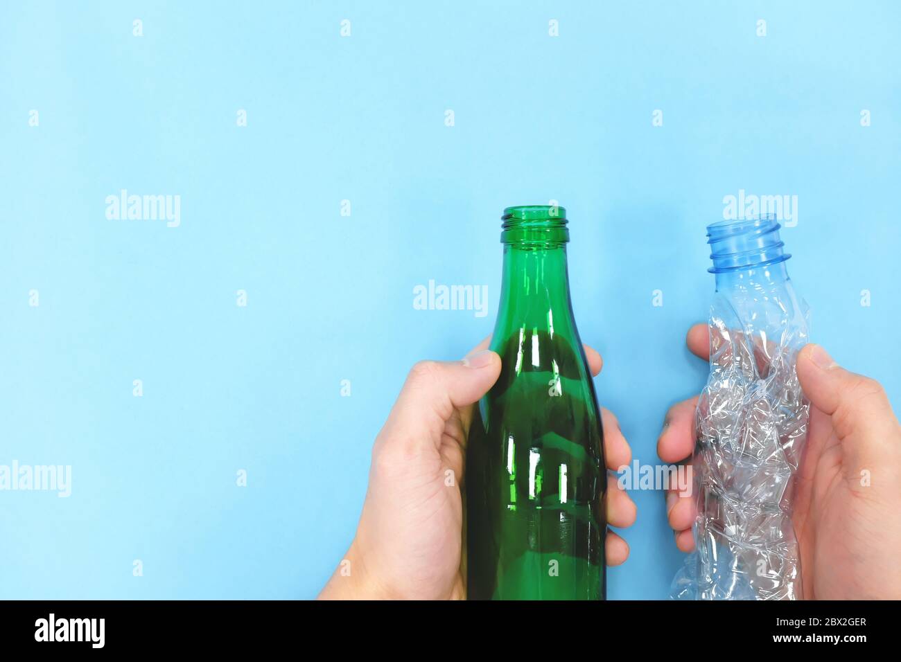 Hands holding empty plastic and glass bottle in blue background. Go