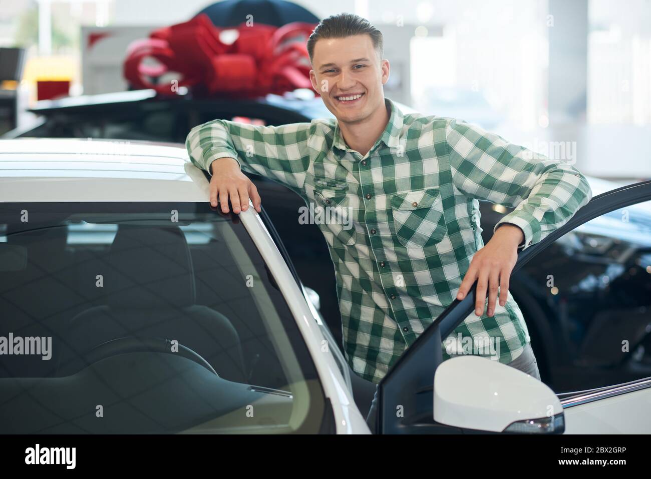 Portrait of handsome smiling man posing, leaning on new car with door