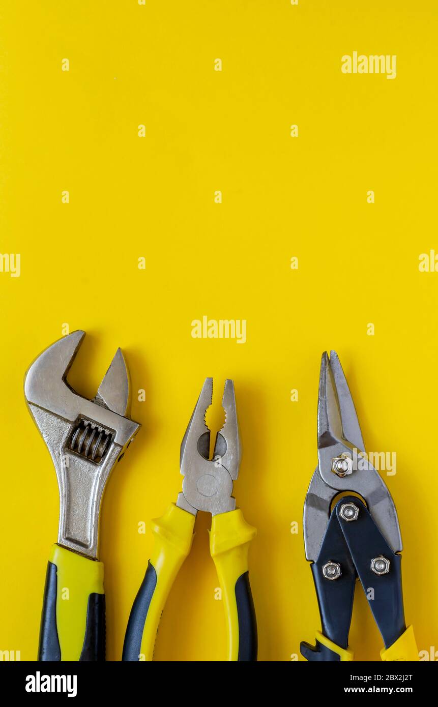 Line of hand tools with black and yellow handles on a yellow background ...
