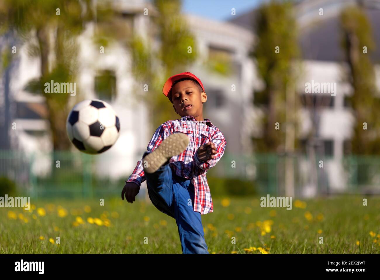Little boy shooting at goal.Young african american soccer player kicking a football ball on a grass field. Stock Photo