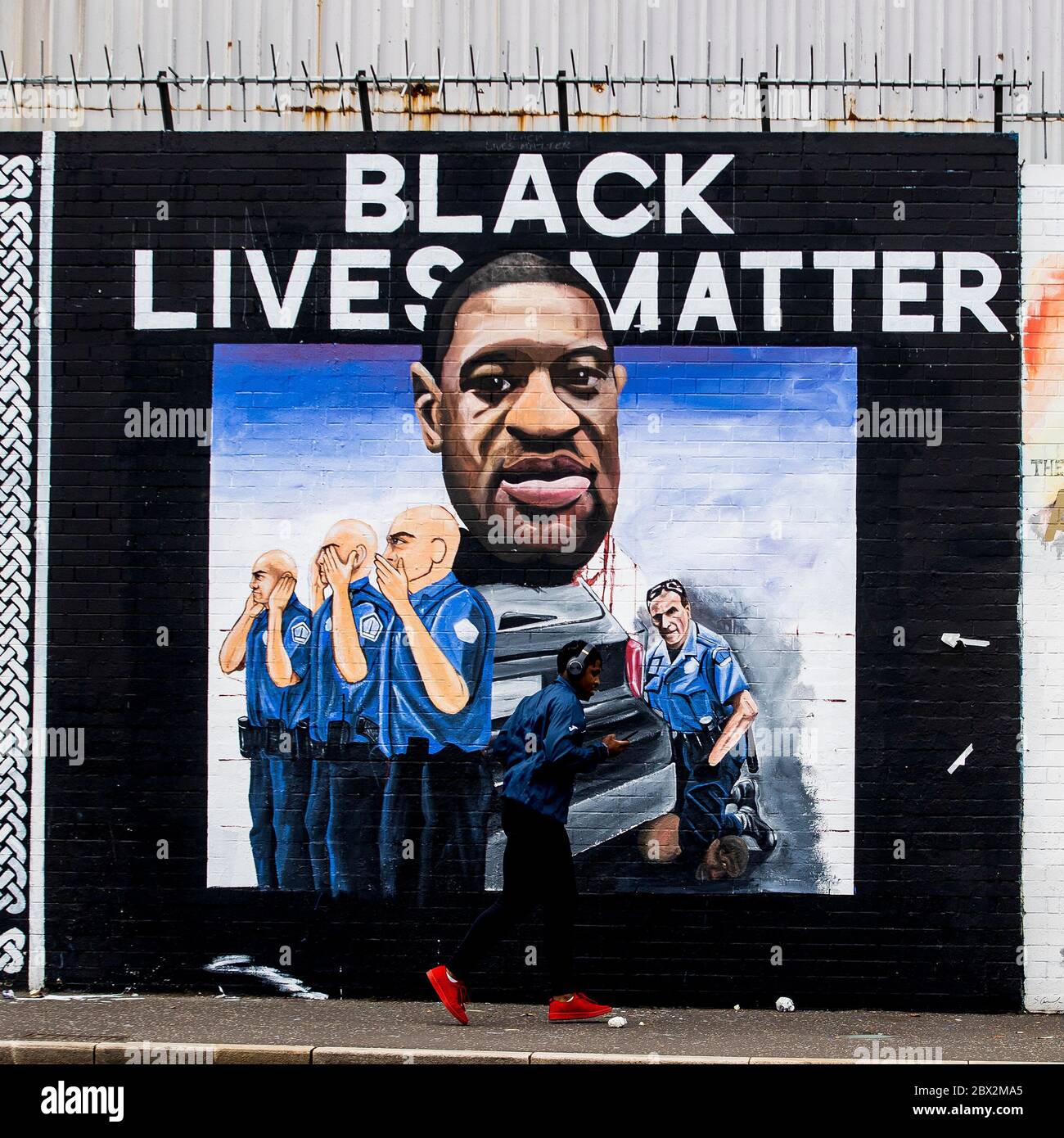 NOTE CONTENT ON MURAL A jogger passes a newly painted mural to George Floyd at Belfast's International Wall. Mr Floyd died after a white officer held him down by pressing a knee into his neck last Monday. The mural was commissioned by Feile an Phobail and Failte Feirste Thiar, and painted by Marty Lyons and Mickey Doherty. Stock Photo