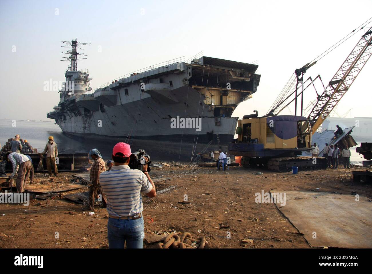 Shipbreaking Yard in Darukhana, Mumbai, India – INS Vikrant dismantling with scrap metal & workers in background Stock Photo