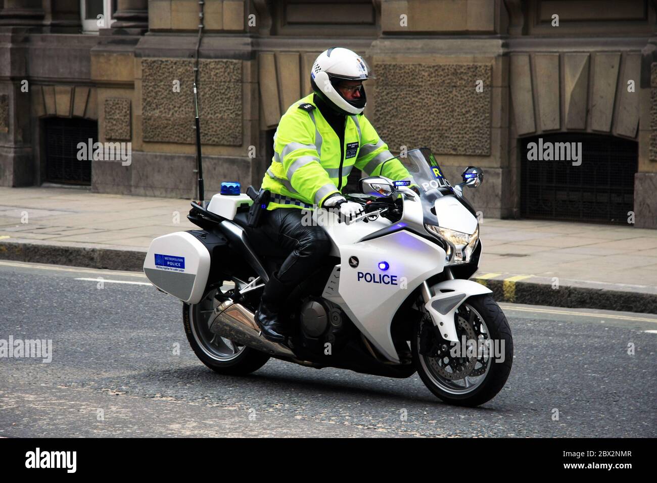 British police officer on a Royal escort police motorbike driving through London street scene with flashing blue lights Stock Photo