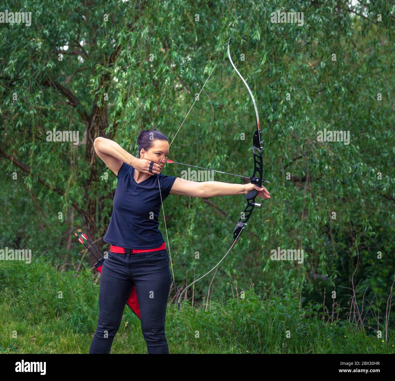 archery in nature. A young attractive woman is training in a bow shot with an arrow at a target