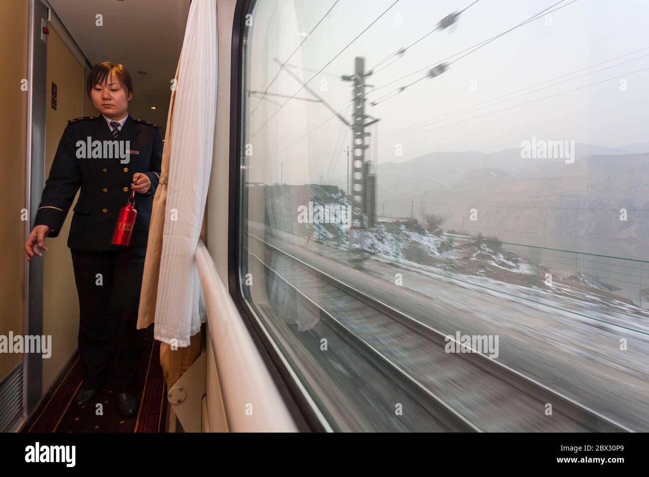 China, Gansu province, near Lanzhou, young female conductor in uniform walking in a corridor of the train bound for Lhasa and view of the frozen countryside through a window, the T27 train leaves from Beijing and reaches Lhasa, Tibet, in 48 hours for 4561 kilometers Stock Photo