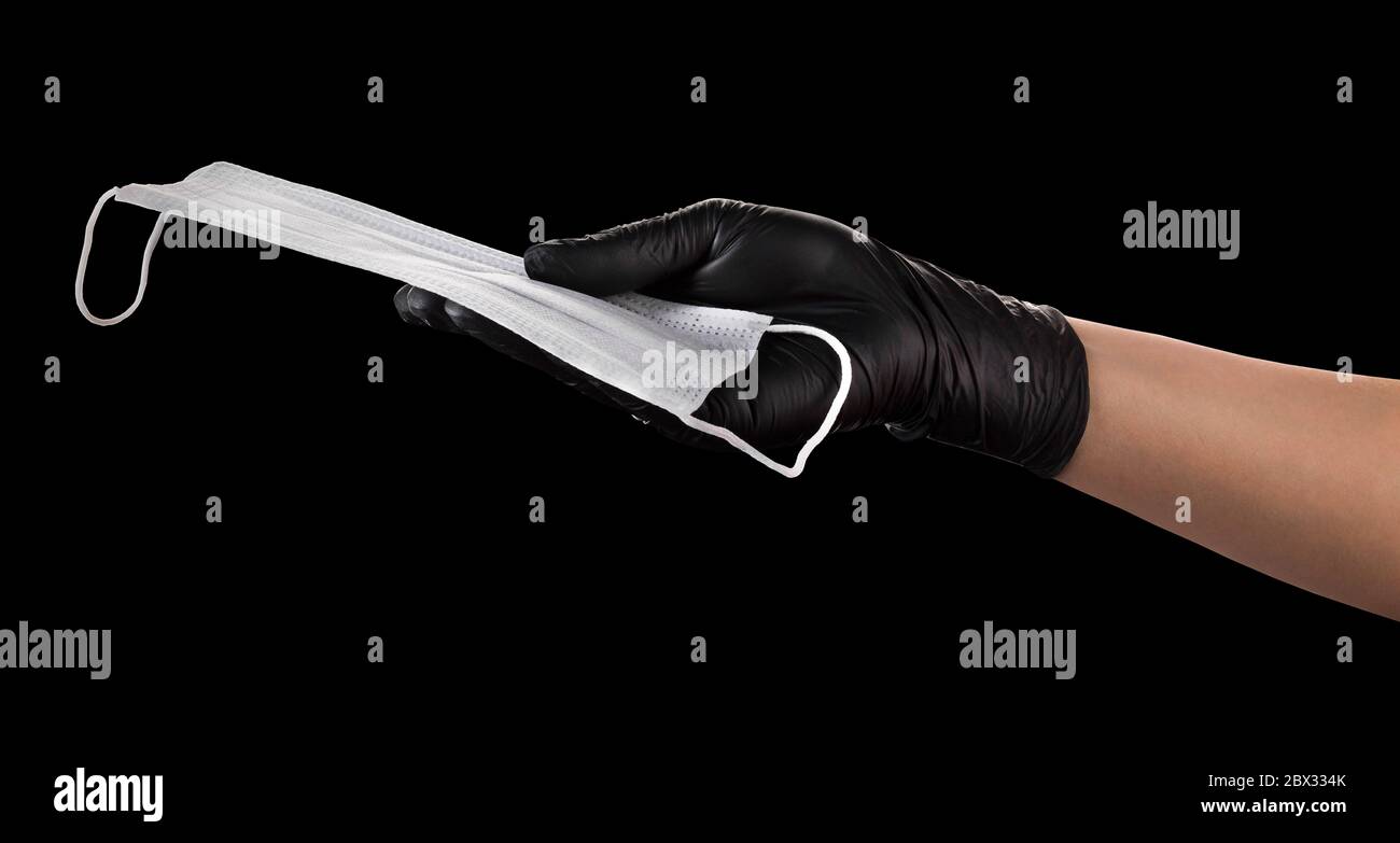 Hand in black gloves holding disposable face mask isolated on black ...