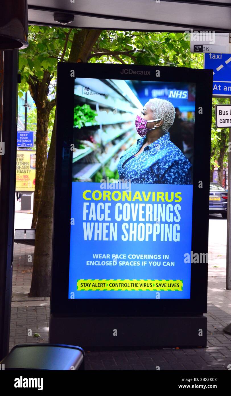 An electronic advertising sign at a bus stop in central Manchester, England, United Kingdom, advises wearing face coverings while shopping to reduce the spread of Coronavirus or Covid-19 during the global pandemic of the infection. Stock Photo