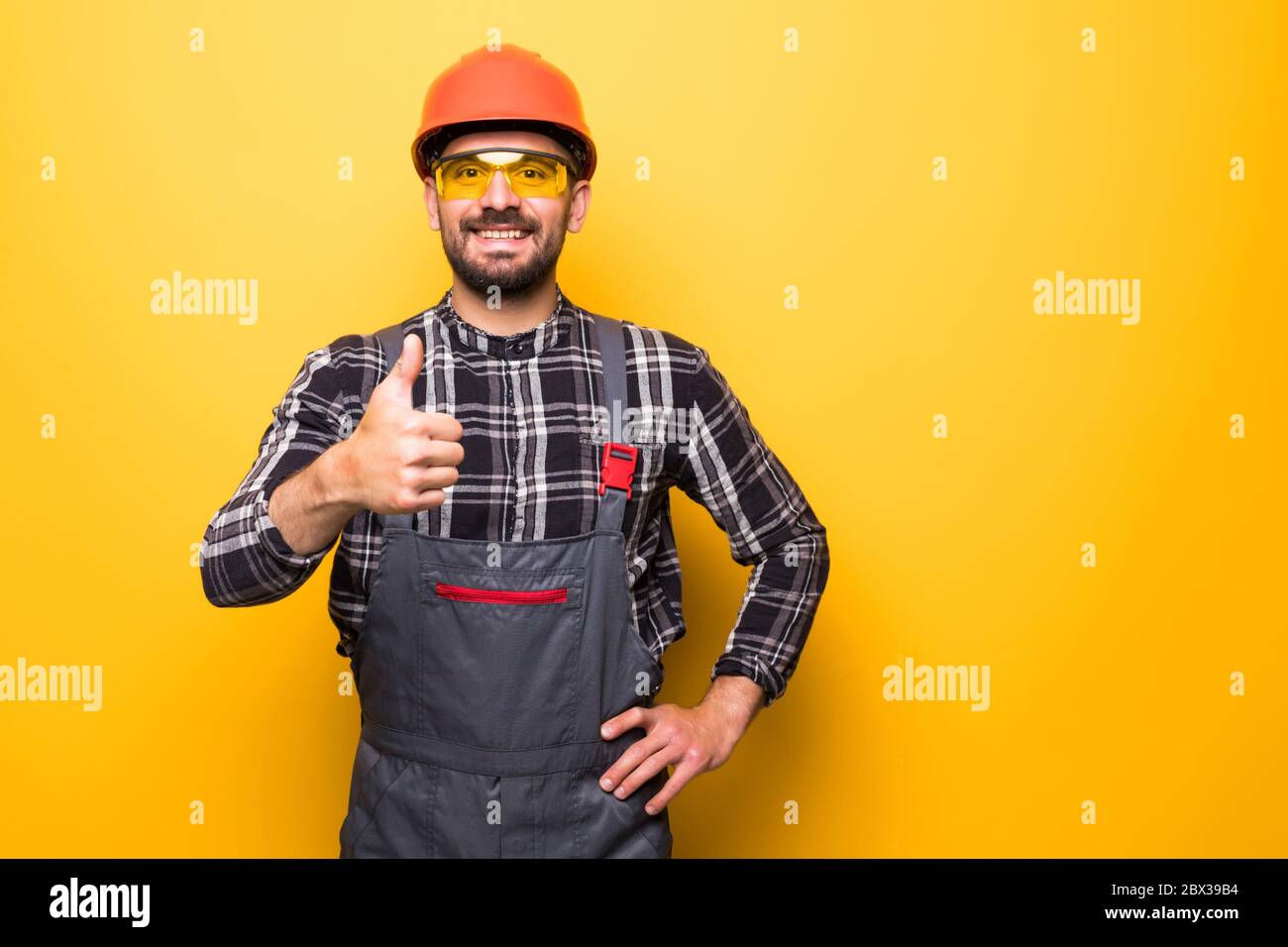 Portrait of a construction worker with hardhat making thumbs up sign on yellow background Stock Photo