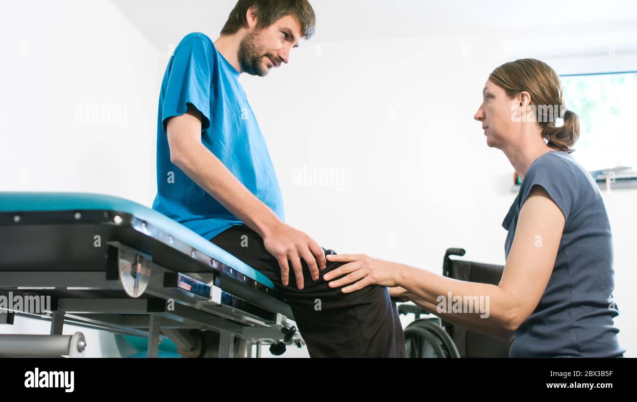 Physiotherapist exercising with disabled person using wheelchair on a therapy table Stock Photo