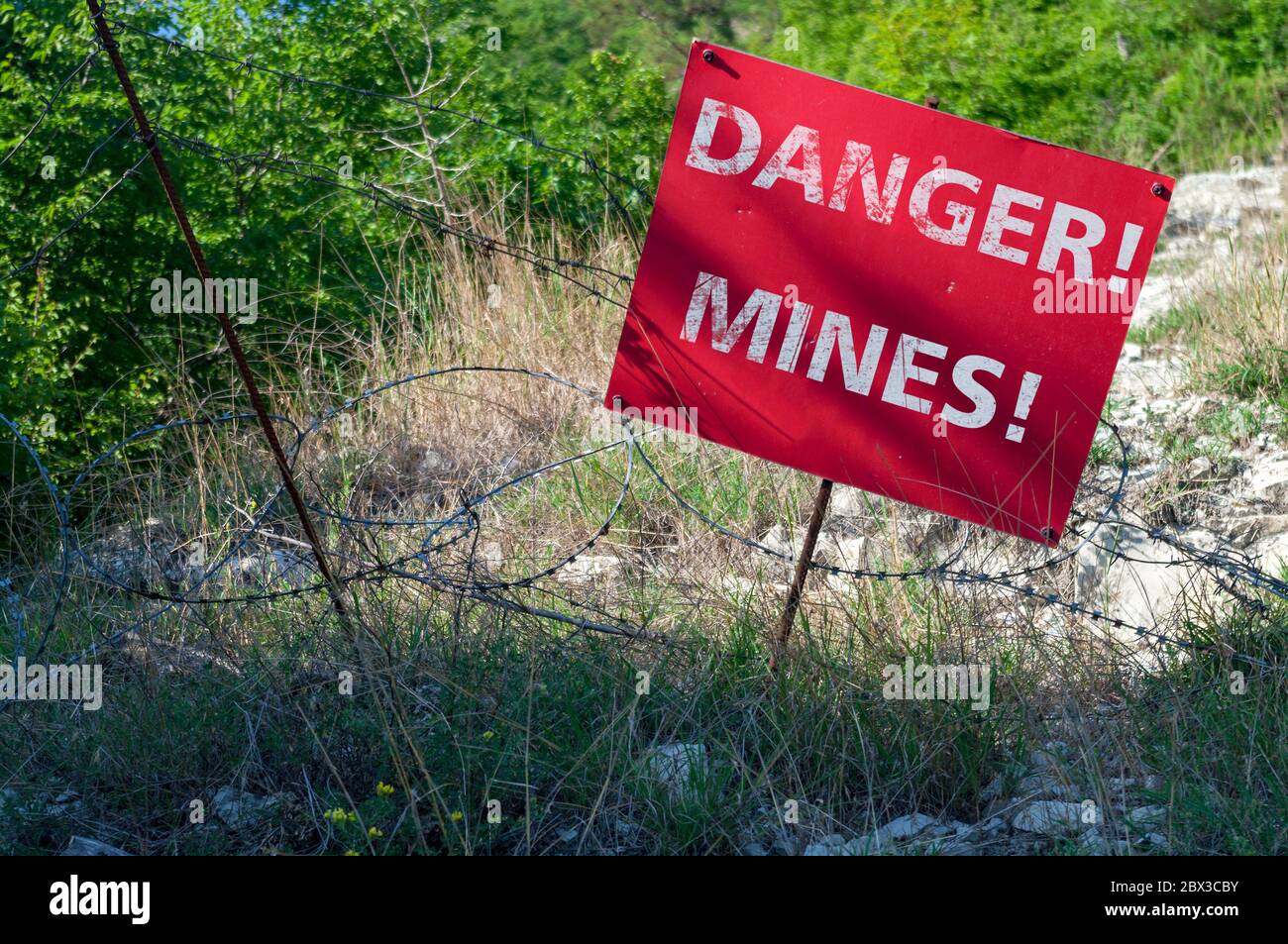 Red sign DANGER MINES in front of a minefield fenced with barbed wire Stock Photo