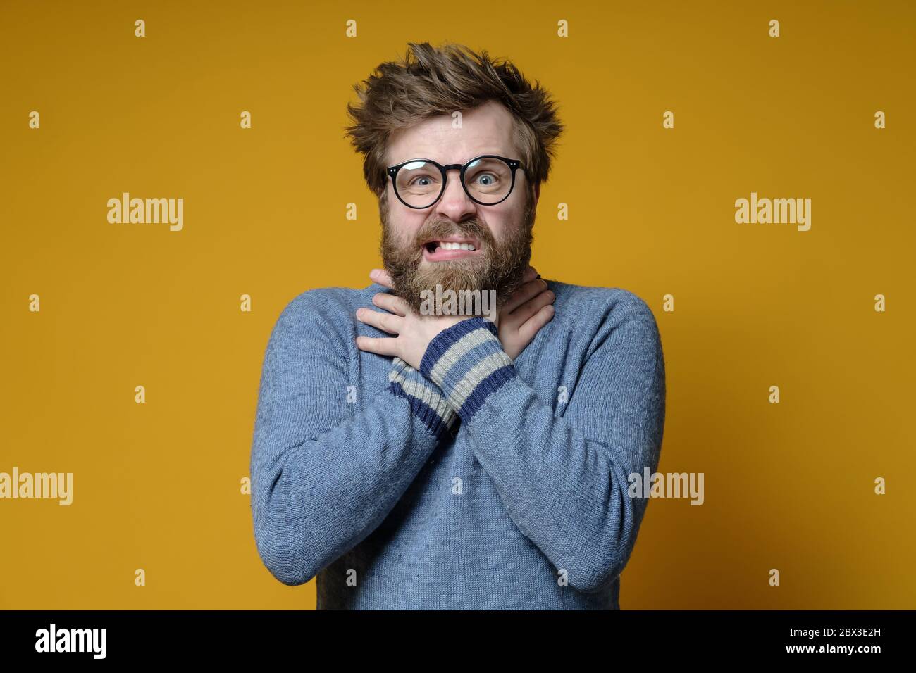 Man with disheveled hair and a beard is under stress, he is crazy, suffocating himself with hands while squeezing neck. Stock Photo