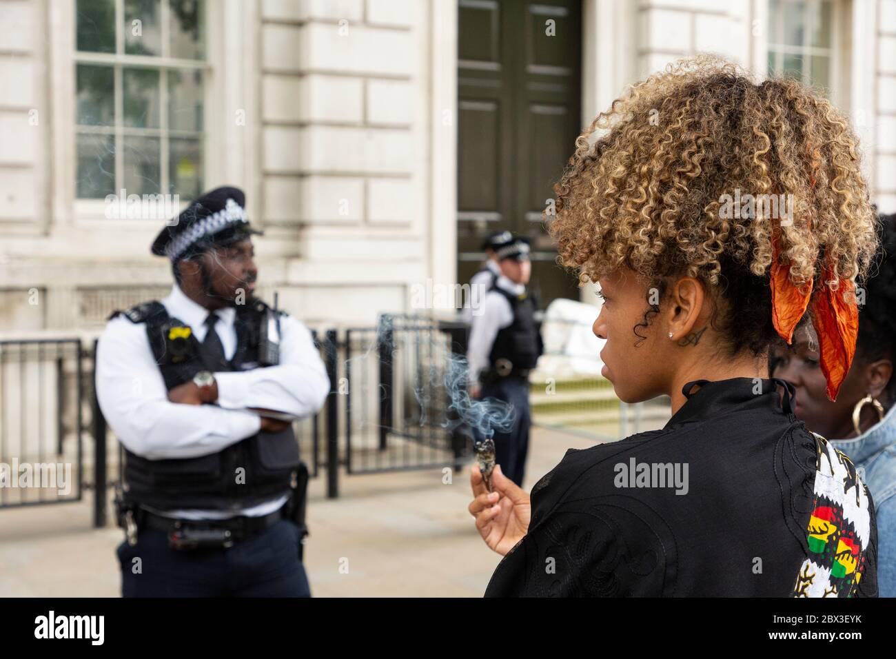 A young protester burns sage in front of a policeman during the Black Lives Matters protest outside 10 Downing Street, London, 3 June 2020 Stock Photo