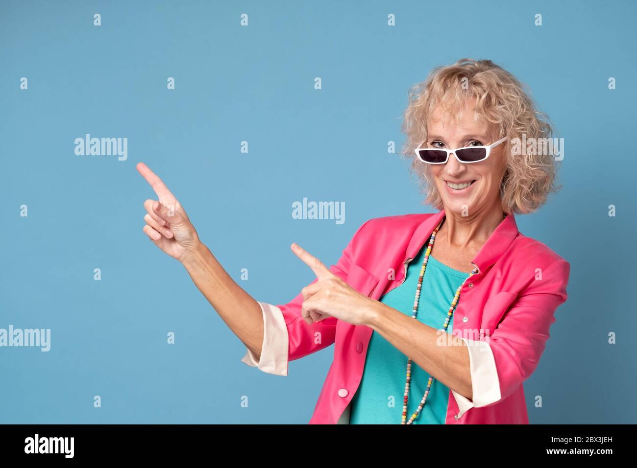 woman with sunglasses smiling cheerfully and pointing with forefingers away Stock Photo