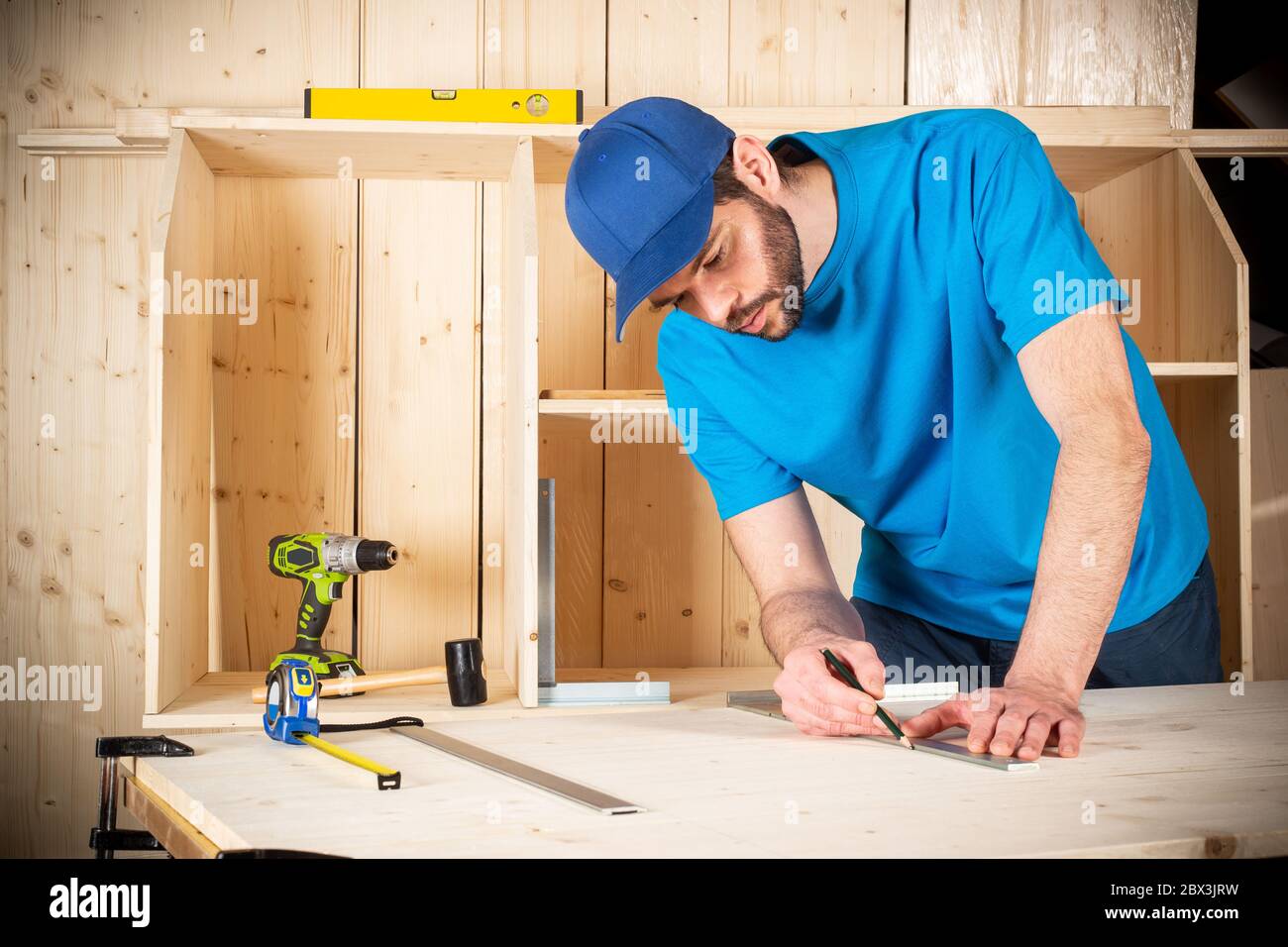 young male carpenter with beard pencil and stop angle meter at work. measuring on wood plank  woodworking construction tool concept furniture making d Stock Photo