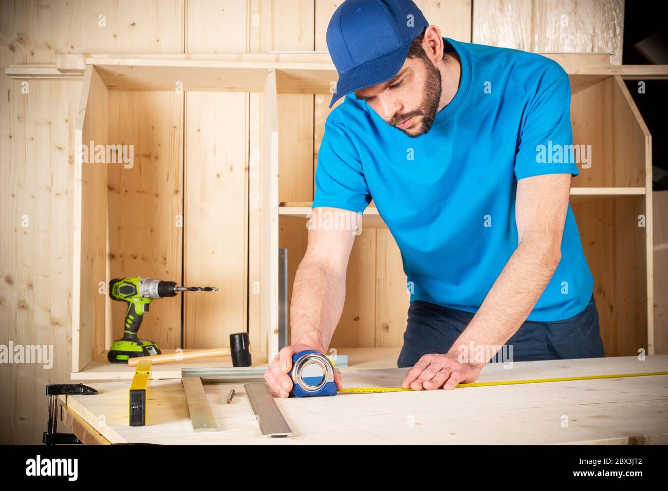 young male carpenter with beard and metal tape measure at work. measuring on wood plank  woodworking construction tool concept furniture making diy ba Stock Photo