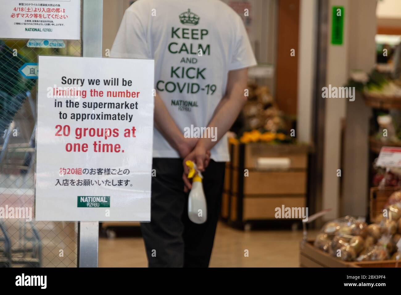 A sign outside a supermarket in Hiroo in central Tokyo, Japan informs customers only 20 groups are allowed at one time to follow social distancing guidelines, while a person wears a shirt with a defiant slogan reading Keep Calm and Kick Covid-19 during an outbreak of COVID-19 coronavirus, April 29, 2020. Photographer credit Niclas Ericsson. () Stock Photo