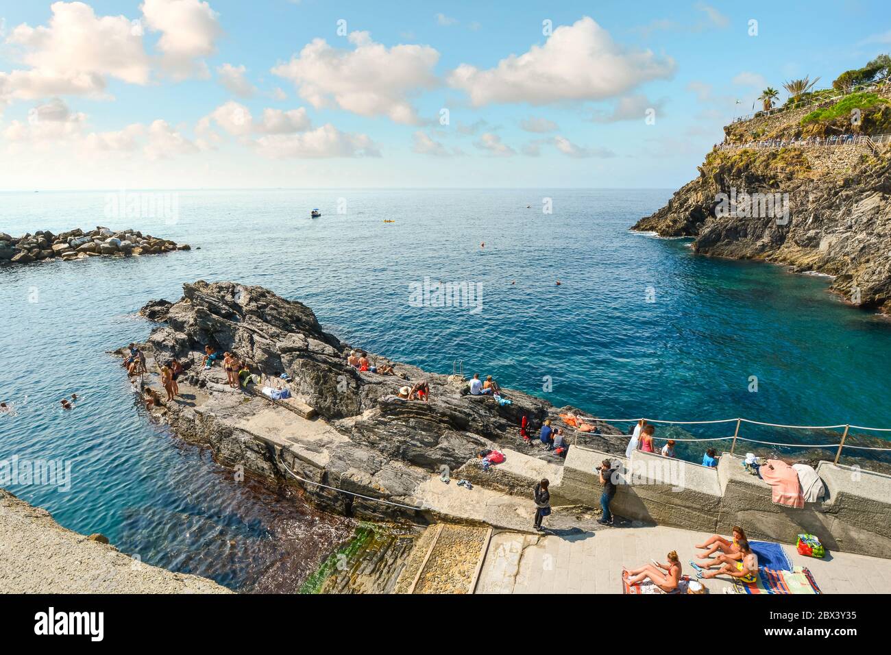 Tourists swim in the sea and sunbathe near the the rocky coastline of Manarola, Italy, part of the Cinque Terre. Stock Photo