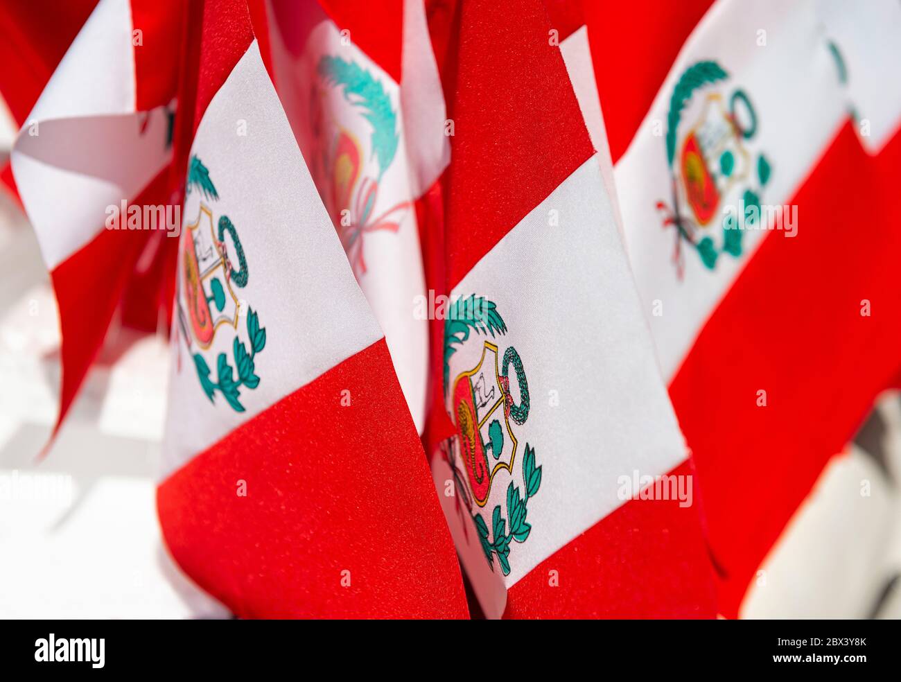 Small Peruvian flags for sale on the national day, Cusco, Peru. The central coat of arms with vicuna, cinchona tree and cornucopia with coins spilling. Stock Photo