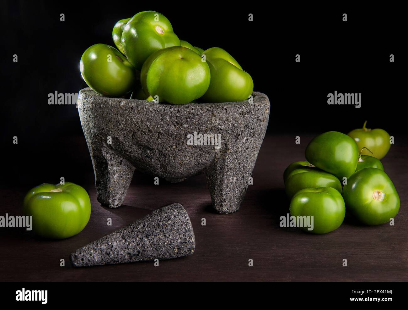 A bunch of Tomatillos or husk tomato in a molcajete in dark food photography in a black background on a wooden rustic table. Concept of Mexican food. Stock Photo