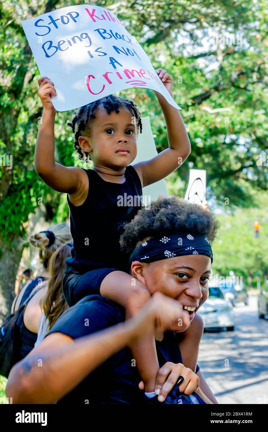 An African-American boy holds a sign as he sits on his mother’s shoulders at a protest against police brutality, June 4, 2020, in Mobile, Alabama. Stock Photo