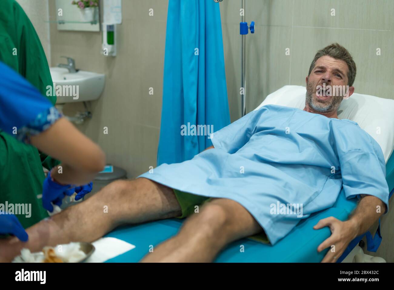 anonymous doctor treating leg wound of scared and worried man in pain at hospital room - injured man lying on bed suffering painful problem feeling si Stock Photo