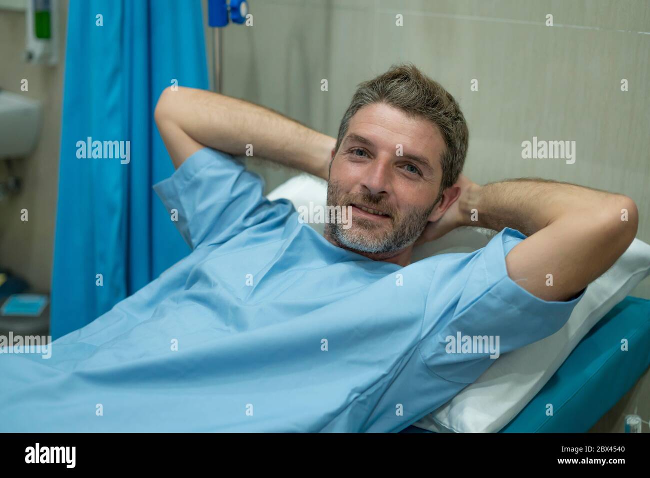 young attractive and trustful man in hospital patient gown lying on clinic bed responding to treatment and healing feeling relaxed feeling positive an Stock Photo