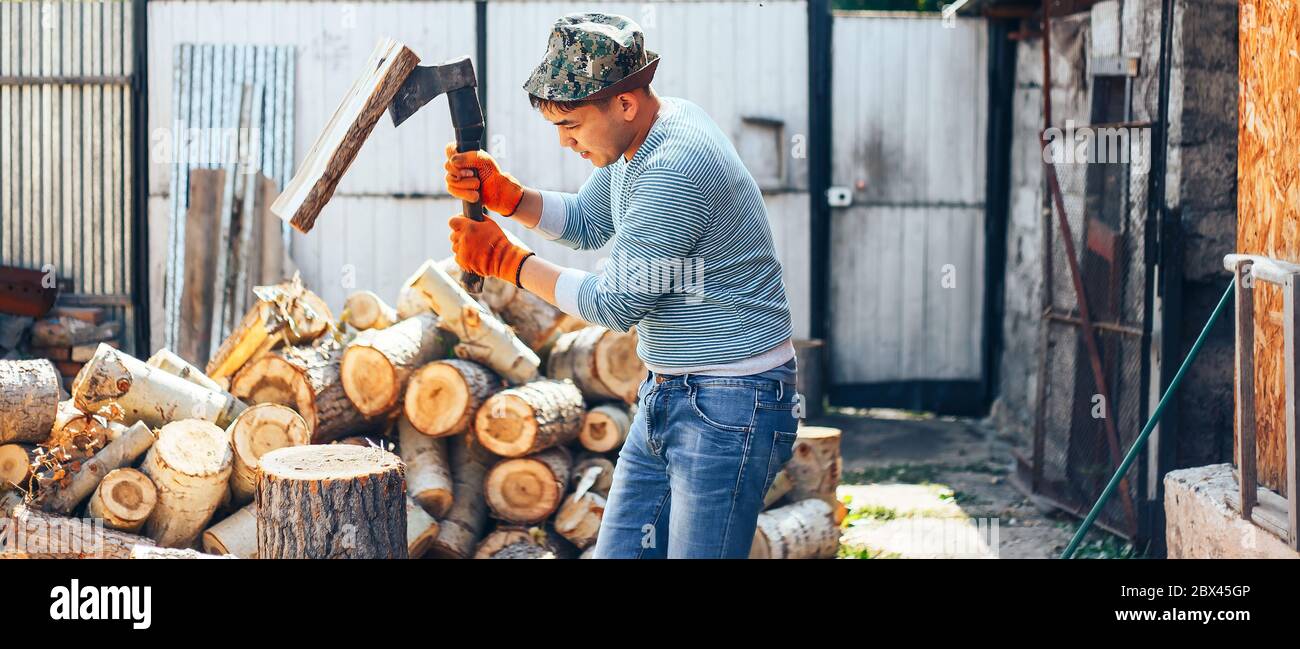 Man in jeans and checkered shirt standing near stump with ax in hands long banner Stock Photo